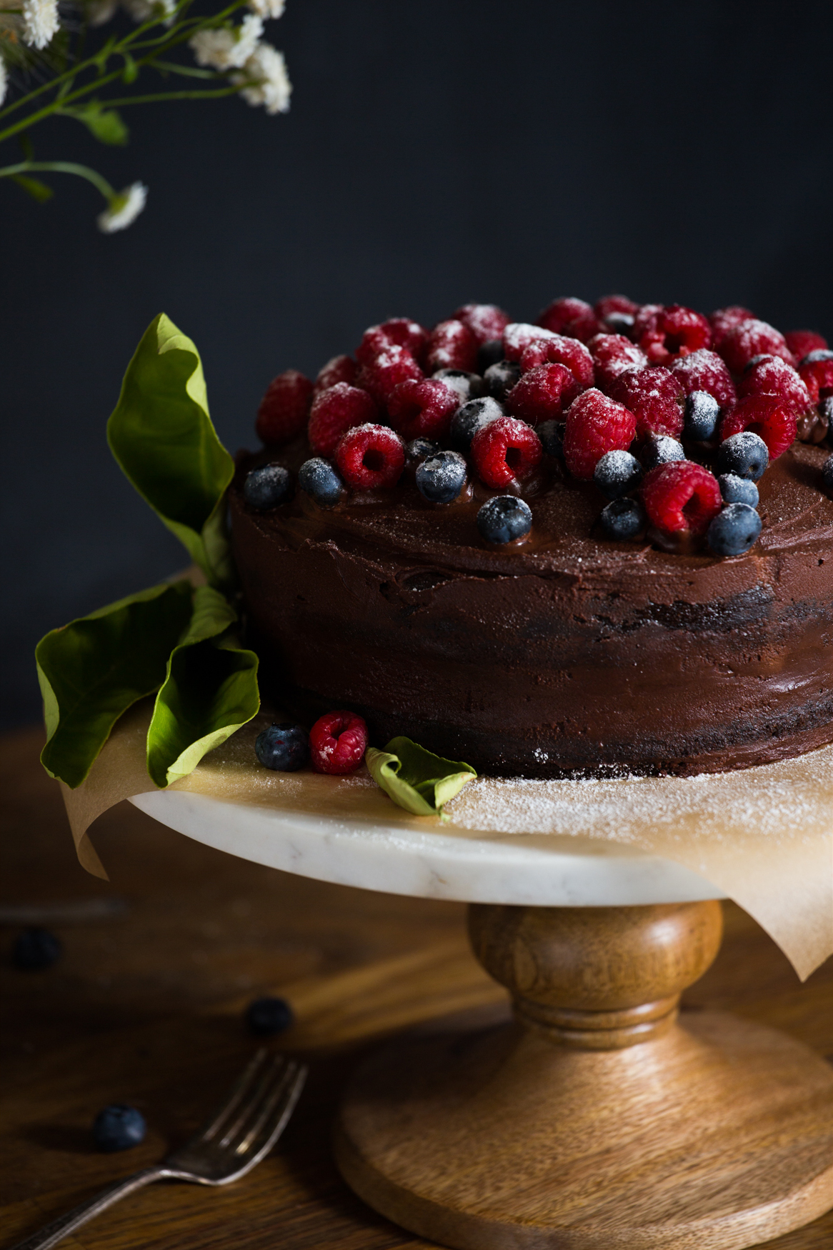 Food propping, moody kitchen setting with a finished chocolate cake dressed with berries