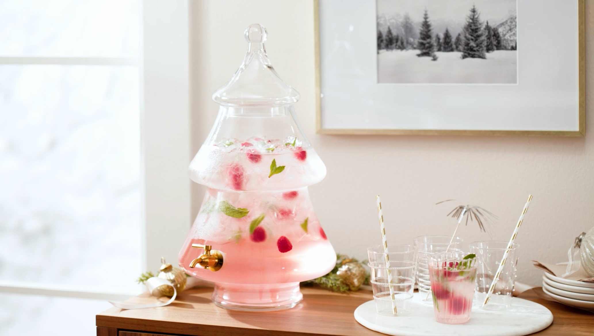 Tree shaped glass drink dispenser with a raspberry mint drink on a wood buffet
